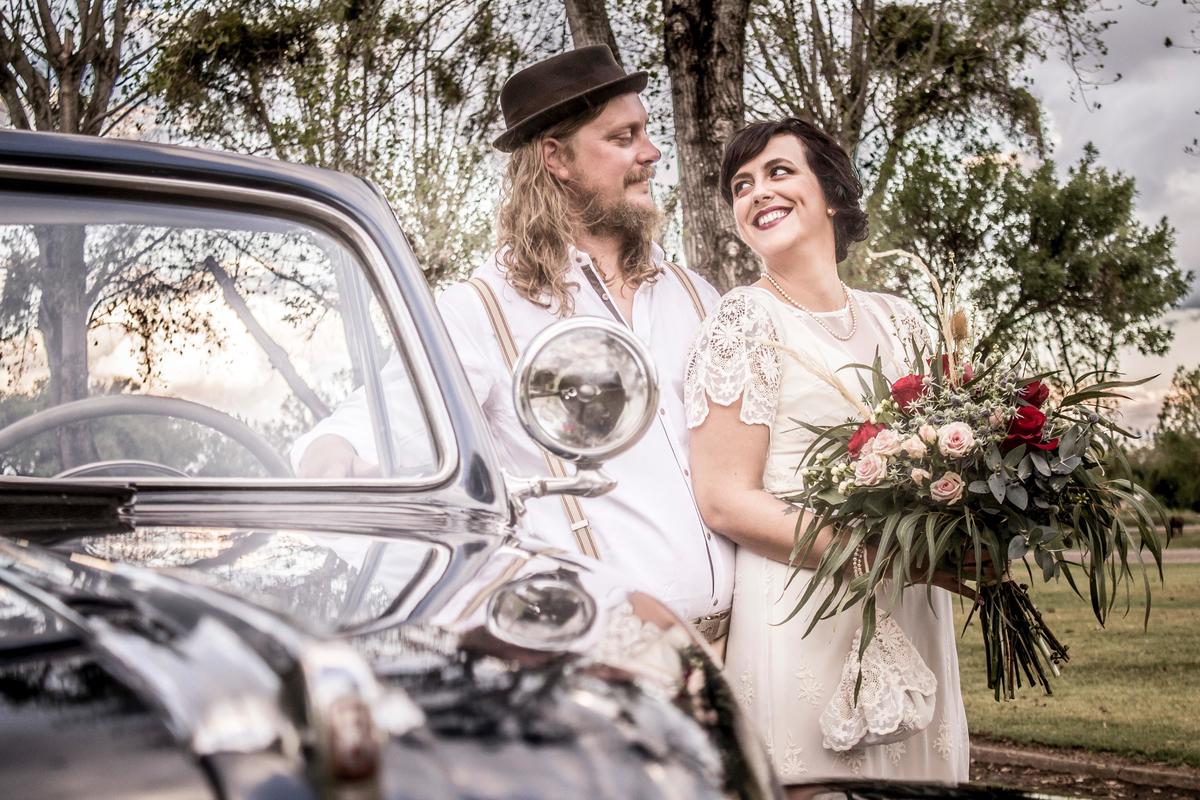 Phtographie d'un couple marié devant leur voiture de mariage