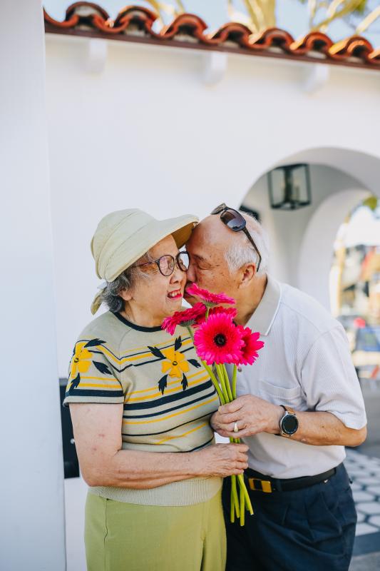 photographie d'un couple de personnes âgées s'embrassant avec un bouquet de fleurs