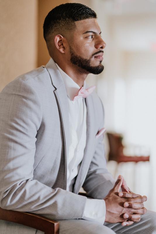 Un marié le jour de son mariage avec un costume gris clair, un noeud papillon rose et un mouchoir de poche rose