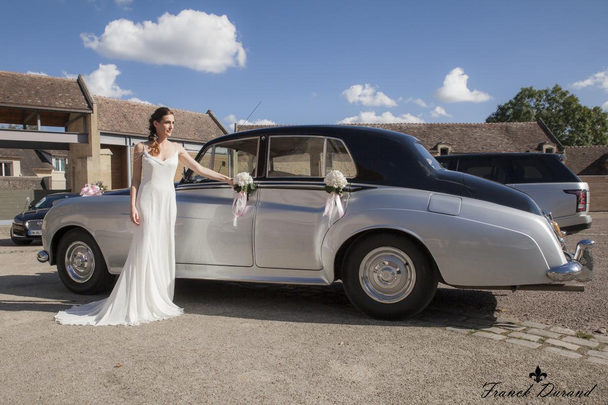 photographie d'une mariée en robe blanche devant la Roll Royce décorée de fleurs des Voitures Henri Pavard