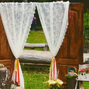 une décoration extérieur pour des photos ou le vin d'honneur, style champêtre avec une arche et des rideaux blancs  - Mariage en Normandie